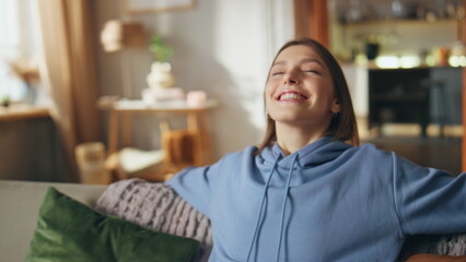 Fototapeta premium Dreamy girl sitting sofa with cheerful smile closeup. Happy woman relaxing couch