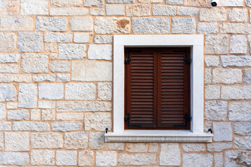 Closed wooden shutters on windows against rustic stone wall background. Traditional Mediterranean architecture concept, vintage exterior design and textured stonework. High quality photo