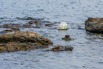 Styrofoam float in ocean water beside large rocks near shore.