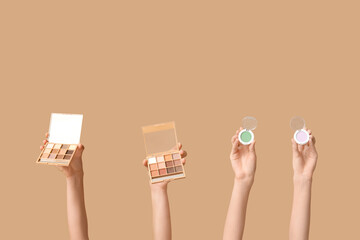 Female hands with different palettes of eyeshadows on brown background