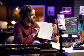 Young artist pointing at music sheet notes to explain on piano keys, teaching people how to play electronic keyboard in home studio. Musician singer playing midi controller keys, master class.