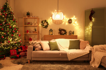 Interior of festive living room with grey sofa, Christmas tree and glowing lights at evening