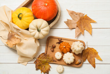 Composition with fresh pumpkins, autumn candles and fallen leaves on light wooden background