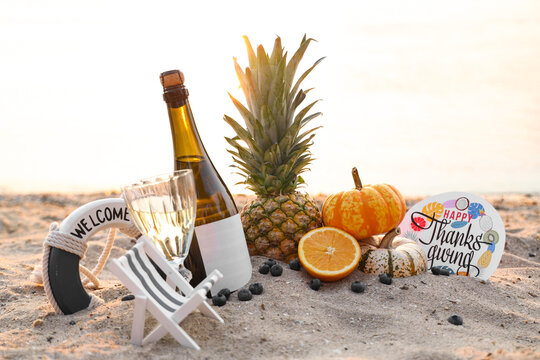 Pumpkins, tasty food, wine and greeting card with text HAPPY THANKSGIVING DAY on beach