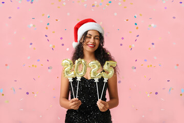 Happy African-American woman in Santa hat and with figure 2025 made of balloons on pink background. New Year celebration