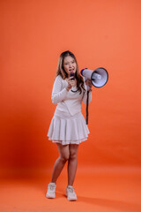 Obraz premium full body beautiful female white top standing screaming angry holding megaphone loudspeaker forward and mic audio isolation orange background. for technology concept, advertising, broadcast, promotion