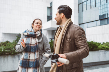 A business man and a woman talking in front of the glass buildings where they work, with an electric bicycle next to them