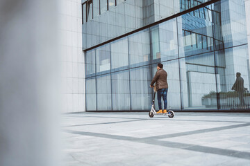 A man rides an electric scooter around the city in front of the glass building where he works