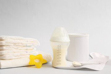 Bottle with baby milk formula, diapers and teethers on light background
