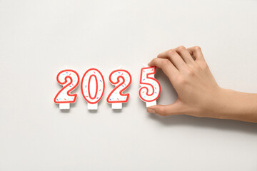 Female hand with candles in shape of figure 2025 on light color background, closeup