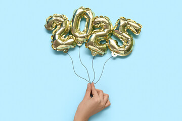 Female hand with foil balloons in shape of figure 2025 on color background