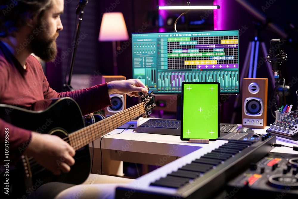Poster musical engineer learning to tune his acoustic guitar before playing, watching online video tutorial