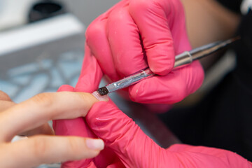 Professional nail technician applying base coat and gel polish using a brush during a manicure session.