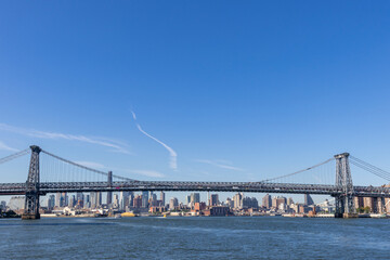 A view of the Williamsburg Bridge spanning the East River in New York City, with urban buildings in the background, showing the city's iconic infrastructure