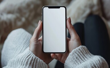 Close-up of a hand holding an iPhone with a blank screen, showcasing winter fashion with a cozy sweater against a blurred urban winter scene