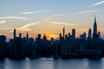 Obraz premium Stunning sunset over the New York City skyline highlighting iconic buildings and reflections on the water