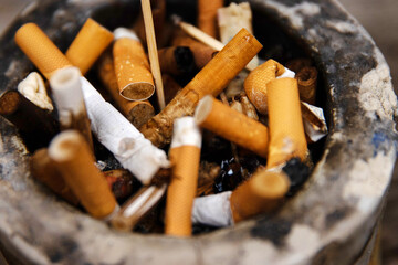 Closeup of an ashtray filled with numerous cigarette butts on a wooden surface, symbolizing smoking habits and litter, smoking harm, urban pollution, unhealthy lifestyle, littering.