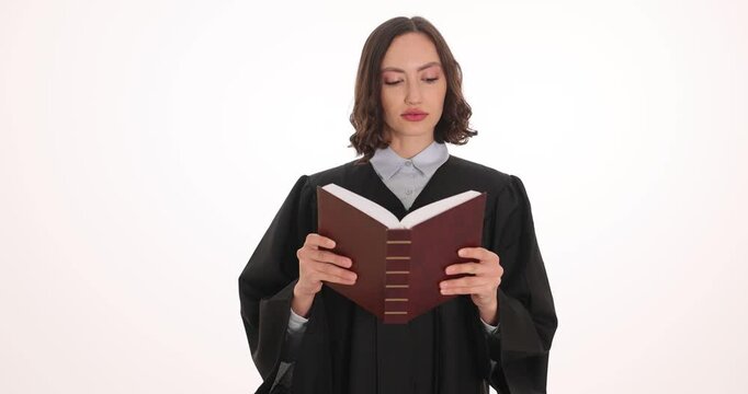 Woman judge in black gown reads laws holding thick corpus juris book on white background. Responsible female improves knowledge in legal field