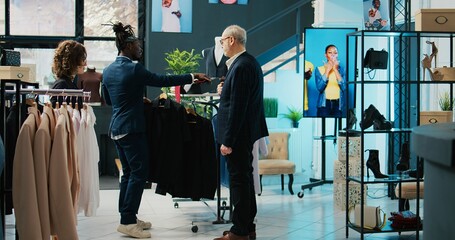 Fashion stylist making trendy recommendations for senior client, pairing an expensive tie to match a black elegant shirt. African american worker selling designer items to man. Camera B.