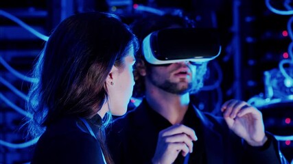 Woman programming in a server room while a man is using a Virtual Reality headset - Powered by Adobe