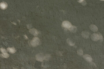 Soft, diffused sunlight creates blurred, rounded shadows on an old textured wall, with varying intensities of light and shadow, producing an abstract, natural background.
