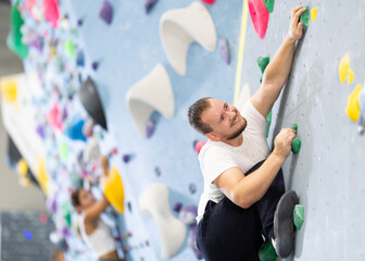 Fototapeta premium Young man in sportswear practicing rock climbing on climbing wall