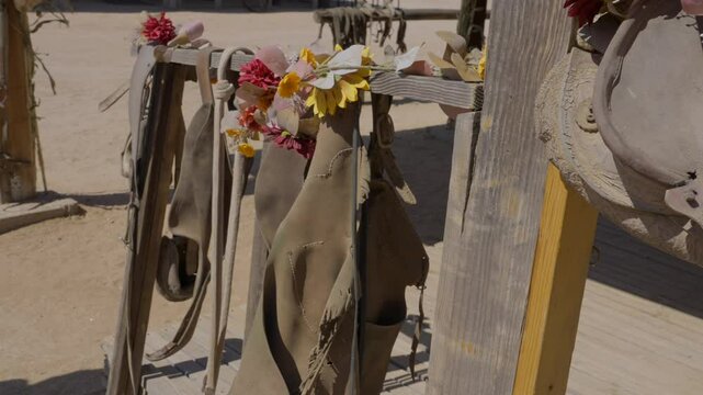 This panning video shows equestrian saddles and chaps hanging on an outdoor railing, adorned with autumn color flowers.