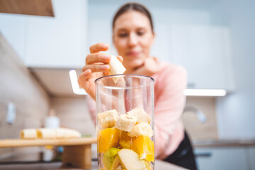 Healthy eating lifestyle concept photo of young woman preparing drink with fruit and vegetables at home in kitchen.