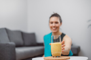 A young woman drinks a vegetable and fruit smoothie in her living room and doing yoga on yoga mat.