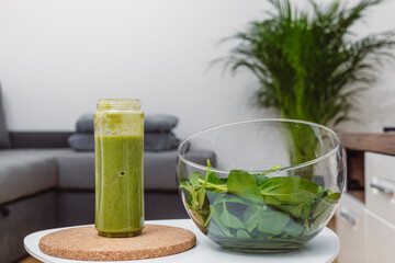 A young woman drinks a vegetable and fruit smoothie in her living room and doing yoga on yoga mat.