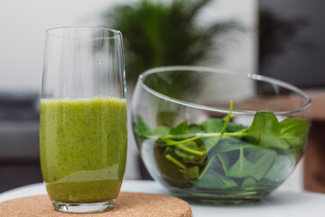 A young woman drinks a vegetable and fruit smoothie in her living room and doing yoga on yoga mat.