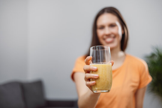 A young woman drinks a vegetable and fruit smoothie in her living room and doing yoga on yoga mat. - Powered by Adobe