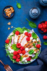 Foodie food salad with fresh raspberries, grilled chicken, feta cheese, red onion, walnuts, spinach and arugula, blue background, top view