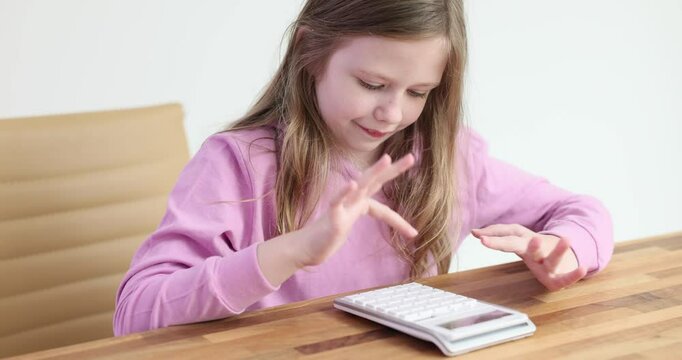 Little girl with curious expression presses buttons on calculator. Concentrated blonde child uses calculator to solve basic math problems