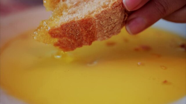 Close up of a woman dipping a piece of bread in an oil plate