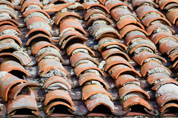 Aged terracotta tile roof with uneven and cracked tiles, showing signs of wear and patches of mortar in between the tiles
