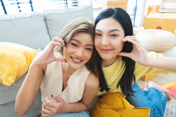 Two Asian women smiling and happy while taking a selfie in their living room at home while making a...