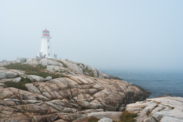 Visitors explore Peggy's Cove Lighthouse on a foggy morning