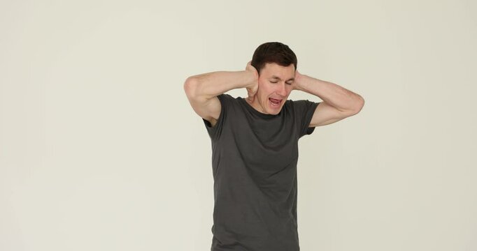 Young man covers ears with hands trying to block out loud noise on white background. Mischief man demonstrates disinterest with gestures slow motion
