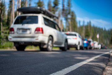 Selective focus on a paved road with a defocused long line of vehicles to enter a national park in the background 