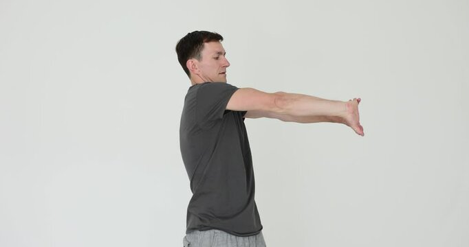 Concentrated man performs arm stretches on white background. Sportsman engages upper body in warm up routine for fitness slow motion. Gym rat