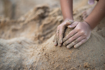 A child is playing in the sand, making a sandcastle