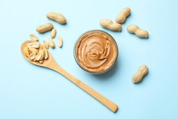 Tasty peanut butter and groundnuts on light blue background, flat lay