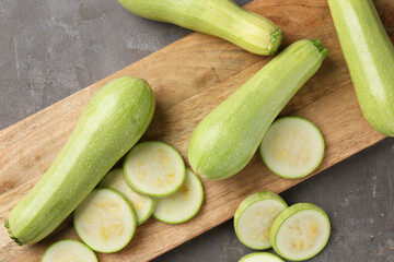 Board with fresh cut and whole zucchinis on grey textured table, flat lay