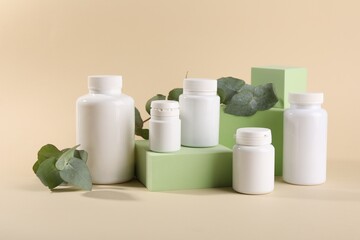 Plastic medical bottles, eucalyptus leaves and podiums on beige background