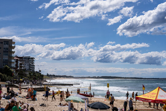 Cronulla Beach in Sydney, New South Wales, Australia, filled with people enjoying a sunny day. Beachgoers are relaxing on the sand, swimming in the ocean, and taking part in various water activities.
