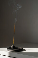 Burning incense stick and smoke with contrast shadows.