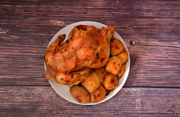 Large plate of delicious lunch, baked new potatoes and whole baked chicken on dark wooden table.