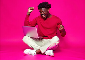 Young black man sitting on the floor with a laptop dancing and having fun