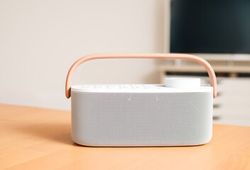 Portable tv speaker or soundbar in front of defocused tv. White modern wireless speaker on table in...